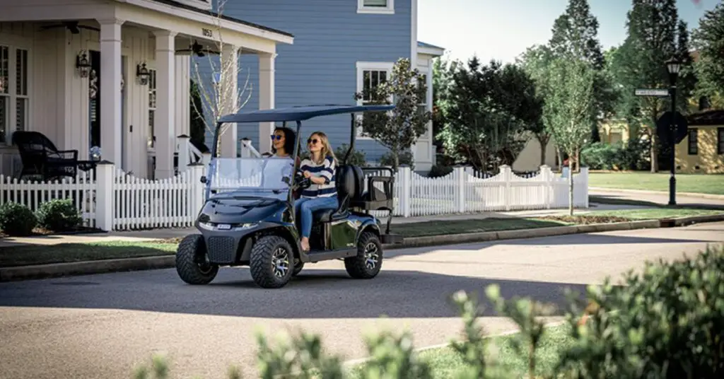 Two women drive an E-Z-GO RXV GAS vehicle down a street.