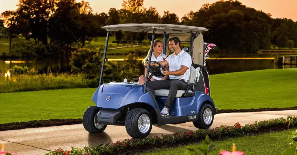 A couple driving a Yamaha Drive 2 gas golf carts on a grassy road